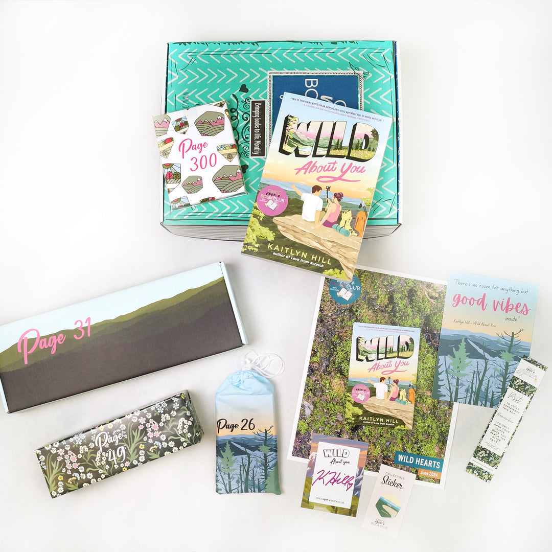 A paperback copy of Wild About You by Kaitlyn Hill sits on a green Once Upon a Book Club young adult box. This box is surrounded by wrapped gifts labeled with page numbers in addition to paperwork including a signed bookplate from the author, bookmark, art print, and matching collectible sticker.