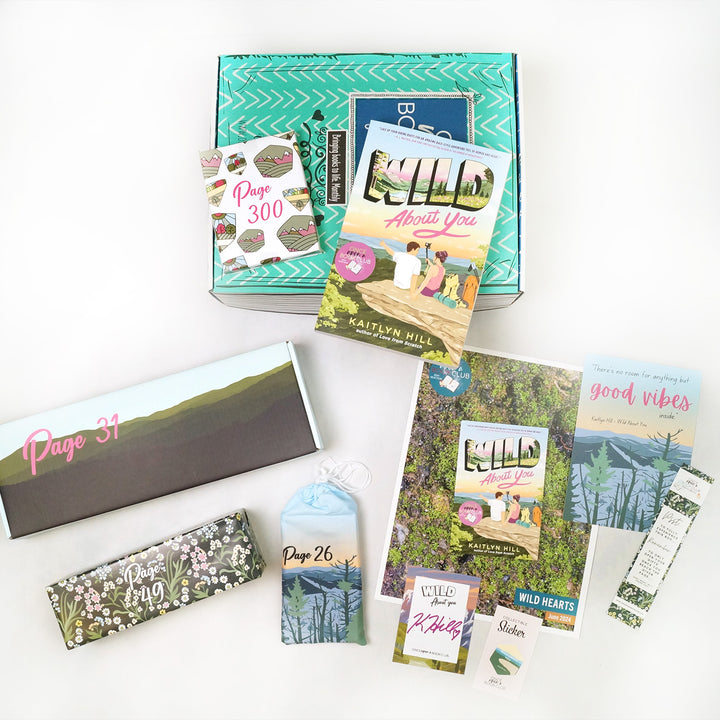 A paperback copy of Wild About You by Kaitlyn Hill sits on a green Once Upon a Book Club young adult box. This box is surrounded by wrapped gifts labeled with page numbers in addition to paperwork including a signed bookplate from the author, bookmark, art print, and matching collectible sticker.