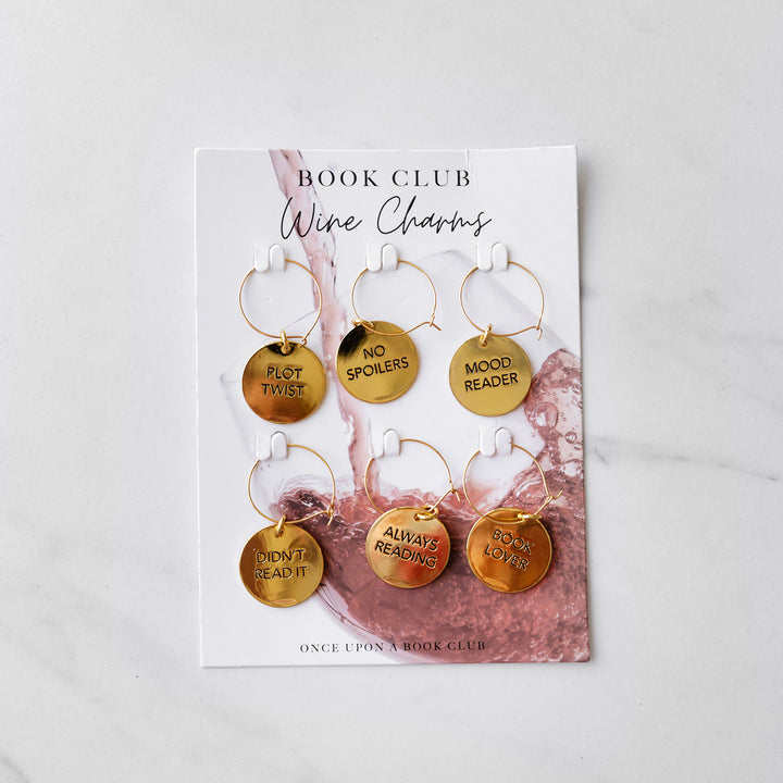 a set of 6 gold wine charms. Each is a book club term including: Plot Twist, No Spoilers, Mood Readers, Didn't Read It, Always Reading, and Book Lover.