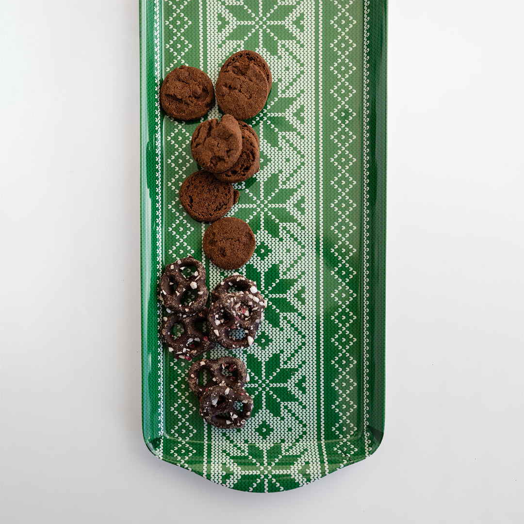 A long green tray with a white snowflake pattern. There are chocolate-covered pretzels and brown cookies on it.