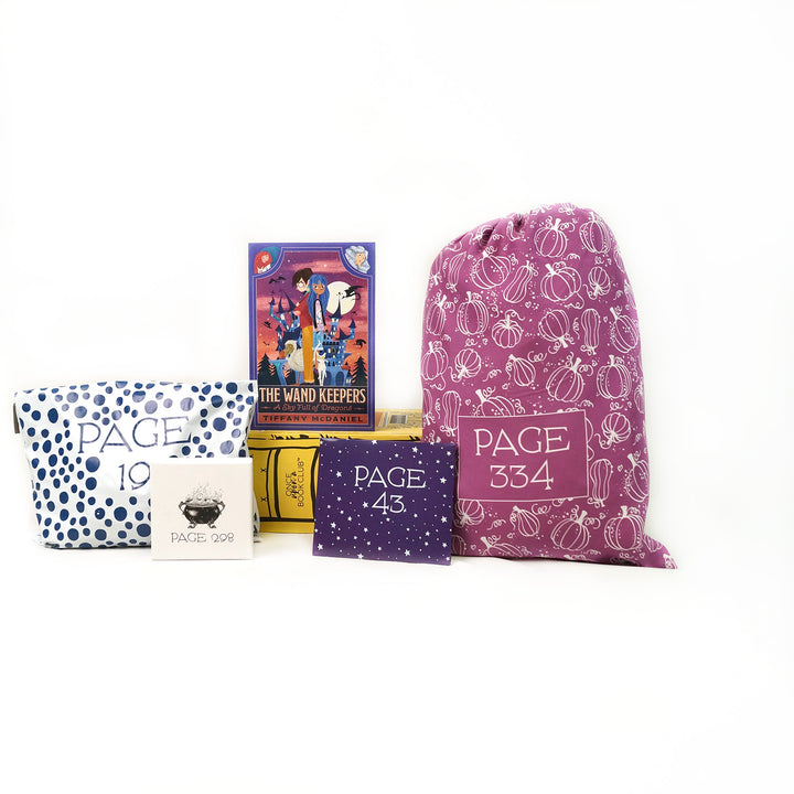 A paperback edition of The Wand Keepers: A Sky Full of Dragon stands on a yellow OUABC box. In front of the box are four themed wrapped gifts labeled with page numbers.