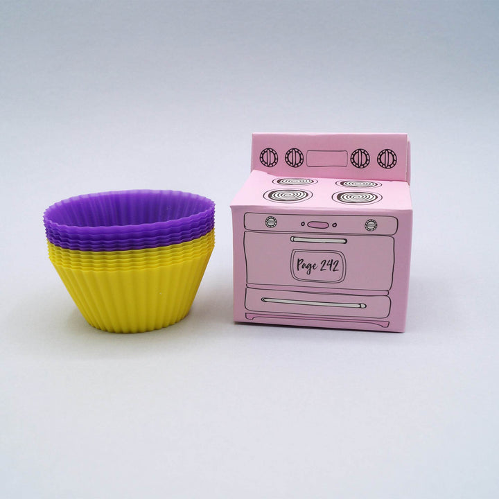 purple and yellow silicone cupcake liners are next to a small pink box shaped like an oven